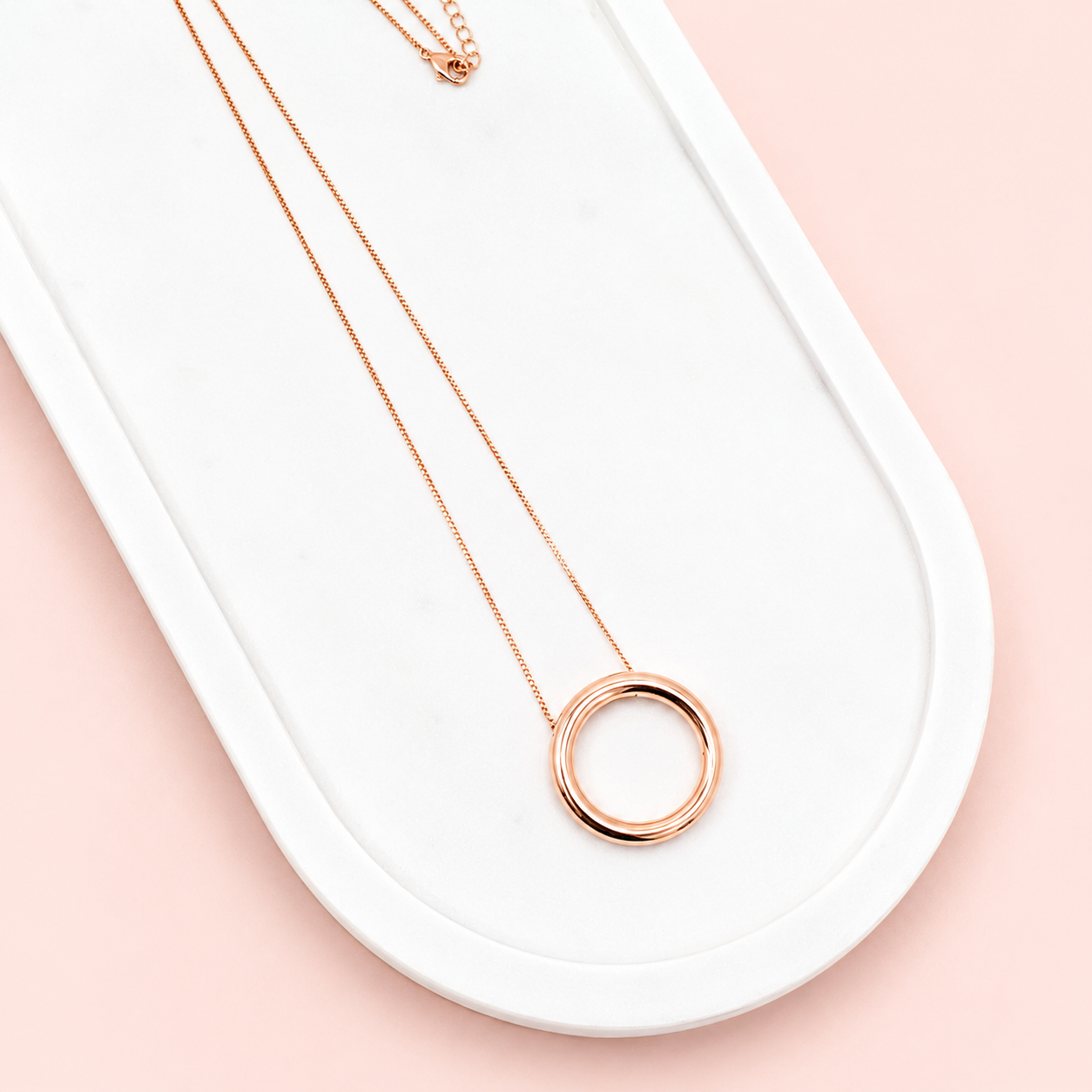 Rose gold necklace with a circular pendant on a white surface.