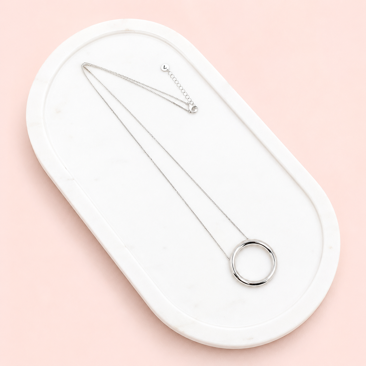 Silver necklace and ring on a white oval tray with a pink background