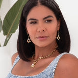 A person wearing a denim dress and showcasing a yellow gold hamsa hand and star charm necklace.