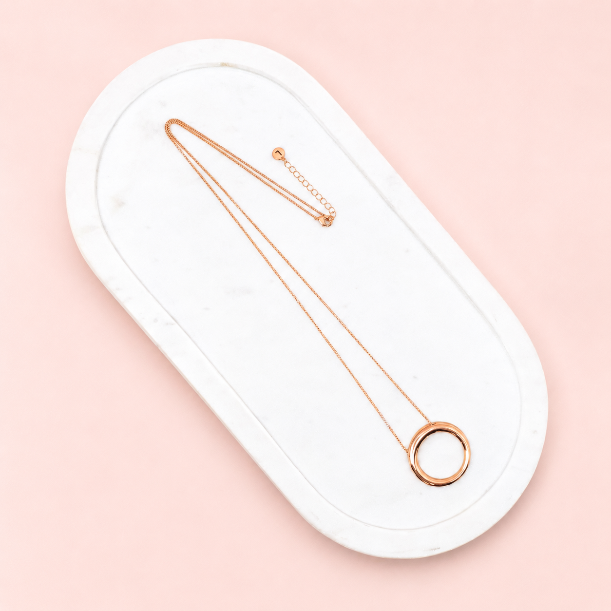 Rose gold necklace on a white oval stand against a pink background
