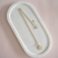 A gold disc necklace with the word 'LOVE' stamped on it, displayed on a white marble surface.