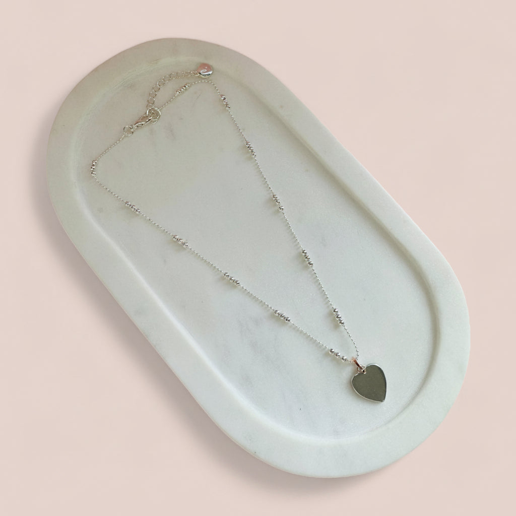 Necklace with a heart pendant on a marble tray against a pink background